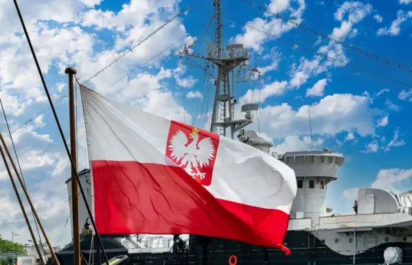 Flaga bandery z orłem dumnie powiewa na tle błękitnego nieba z chmurami, nad pokładem statku.