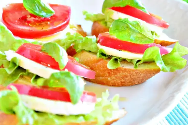Mini kanapki z mozzarellą, pomidorem, sałatą i bazylią na chrupiącej bagietce.