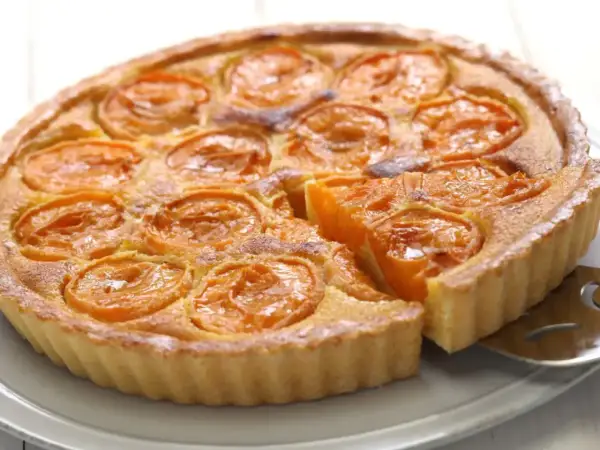 Une délicieuse tarte aux abricots, avec une part déjà servie, révèle sa garniture dorée et ses fruits juteux.