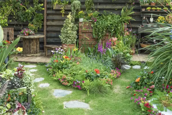 Un jardín exuberante y colorido, con flores vibrantes, follaje verde y un camino de piedras. El mantenimiento de jardinería es clave para esta belleza.