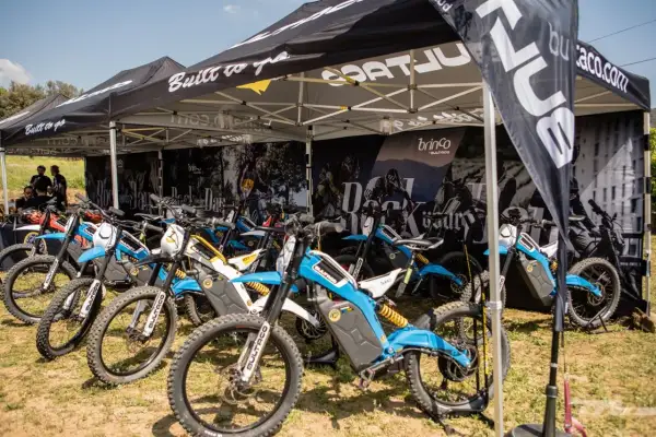 Varias motocicletas Bultaco Brinco eléctricas, de colores azul y blanco, expuestas bajo una carpa.