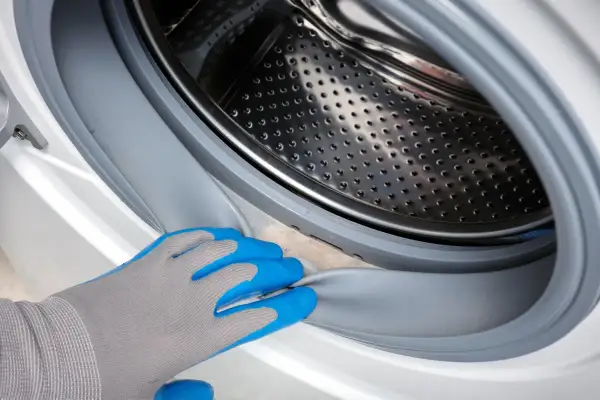 Hand in blue glove cleans the washing machine door seal. A clean ablaufschlauch waschmaschine reinigen is important for hygiene.