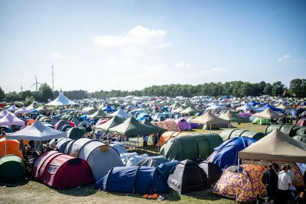 Ein Meer von Zelten beim Roskilde Festival. Menschen entspannen sich im Freien unter blauem Himmel, umgeben von bunten Unterkünften.
