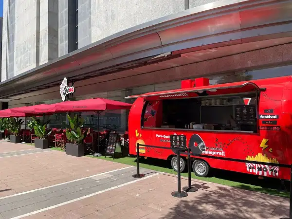 Food truck rojo "Puro Goxis" de Dabiz Muñoz, con "Mamma!!!" y "Alta cocina callejera!!" escrito. Mesas y sombrillas rojas al lado.