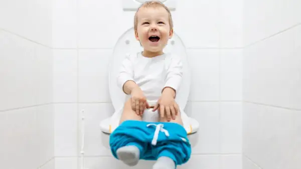 Bambino felice sul water, pantaloni abbassati, pronto per la sua prima cacca nel water.