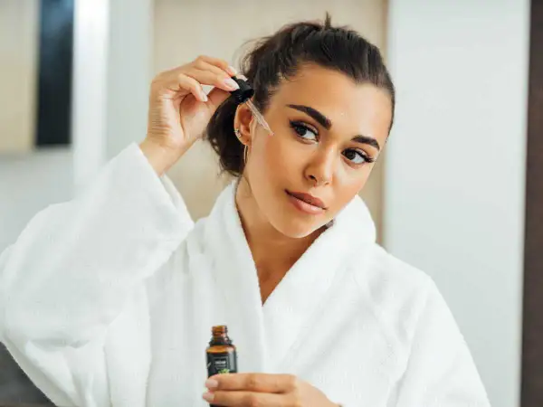 Une femme applique un sérum sur son visage, peut-être un mélange d'acide azélaïque et de vitamine C, pour une peau éclatante.