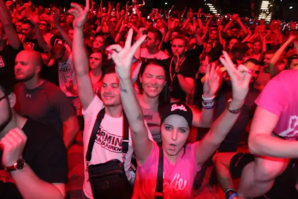 Tłum na koncercie Armin van Buuren Polska, fani pozdrawiają DJ-a, czerwone światła tworzą energetyczną atmosferę.