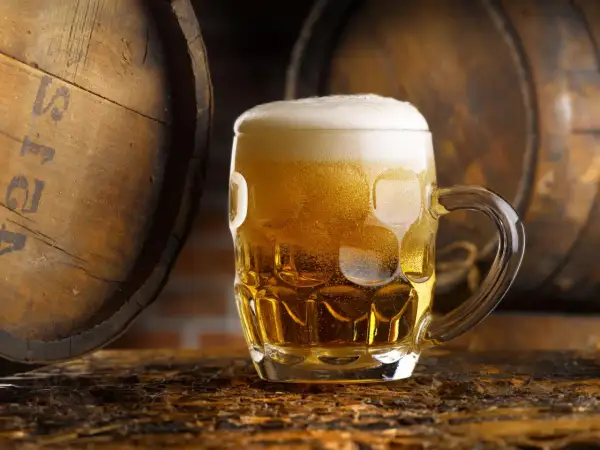 Boccale di birra dorata con schiuma, accanto a botti di legno. Un litro di birra calorie da gustare con moderazione.