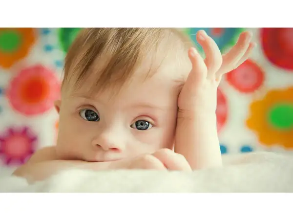 Bambino con sindrome di Down, occhi azzurri, mano sul viso. La vita delle persone Down è piena di amore e gioia.