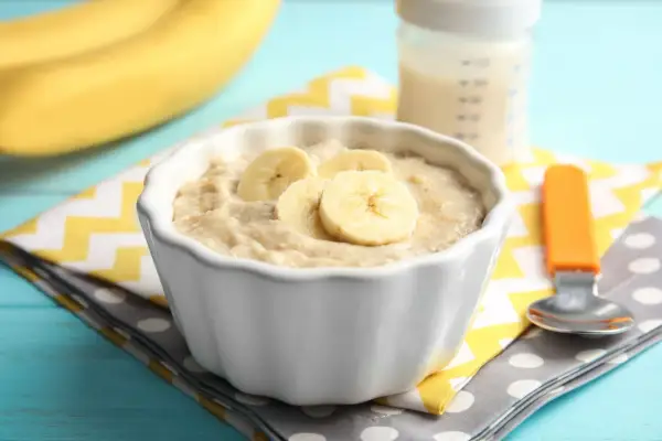 Ein Schüsselchen mit Bananen-Abendbrei, perfekt zum abendbrei selber machen. Daneben eine Babyflasche und ein Löffel.