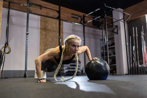 Kobieta wykonuje pompki z piłką lekarską, ćwicząc siłę i wytrzymałość. To świetny sposób, jak trenować crossfit.