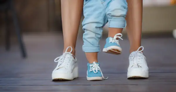 Dziecko w niebieskich bucikach i dorosły w białych sneakersach na drewnianym tarasie.