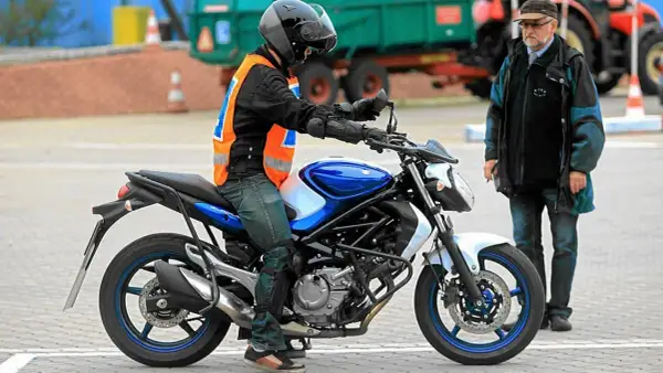 Młody motocyklista w kamizelce odblaskowej na placu manewrowym, obok instruktor. Zastanawia się, od ilu lat prawo jazdy jest wymagane na motocykl.