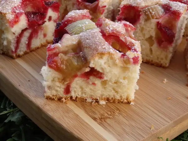 Puszyste ciasto na kefirze z rabarbarem i truskawkami, posypane cukrem pudrem. Idealne na letnie popołudnie.