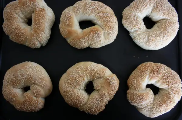 Sex gyllene simit, täckta med sesamfrön, ligger på en svart plåt. Perfekt för ett simit recept!