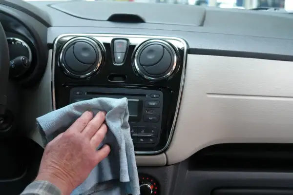 Ręka z szarą ściereczką czyści radio samochodowe i nawiewy. Dbałość o mycie detali w aucie.