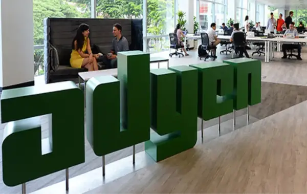 Zielone, przestrzenne litery z napisem "adyen" w nowoczesnym biurze. W tle ludzie pracują przy biurkach i rozmawiają.