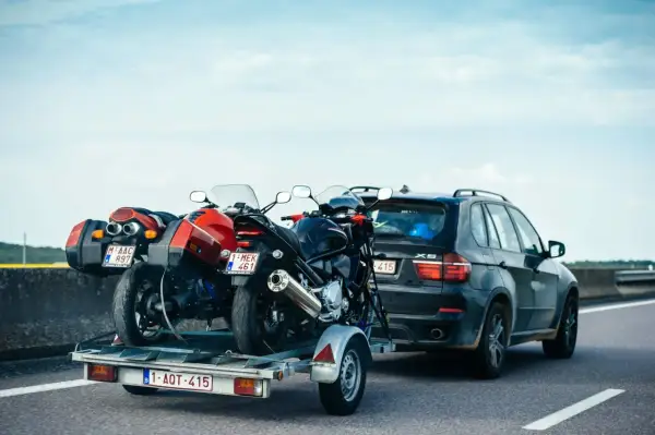 Deux motos sur une remorque tirée par une voiture sur l'autoroute. Le transport de ces véhicules nécessite un permis adéquat pour la catégorie de véhicule tracté.