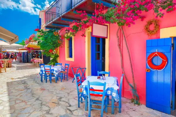 Kolorowa grecka wyspa Kefalonia. Stoliki kawiarniane pod kwitnącymi bugenwillami, niebieskie drzwi i koło ratunkowe.