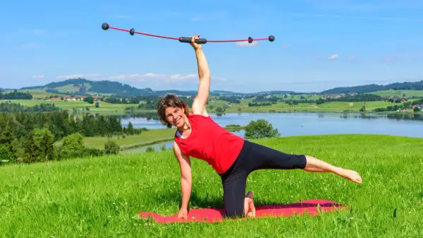 Frau macht Yoga mit einem Schwingstab, dem Testsieger für Balance-Training, vor malerischer Alpenkulisse.