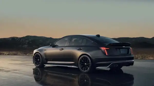 Mroczny Cadillac CT5 z czarnymi felgami i spojlerem na tle górskiego krajobrazu o zachodzie słońca.