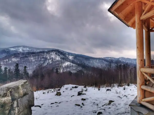 Zimowy krajobraz z ośnieżonymi górami w tle. Na pierwszym planie drewniana altana i kamień. Widok z koziej górki.