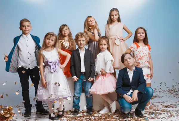Uśmiechnięte dzieci na weselu, ubrane odświętnie, bawią się wśród konfetti.