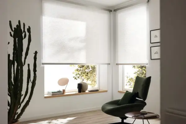 Moderne Sichtschutz-Fenster-Innen-Ideen: Helle Rollos mit dezentem Muster schaffen Privatsphäre und lassen Licht herein. Ein grüner Sessel lädt zum Entspannen ein.