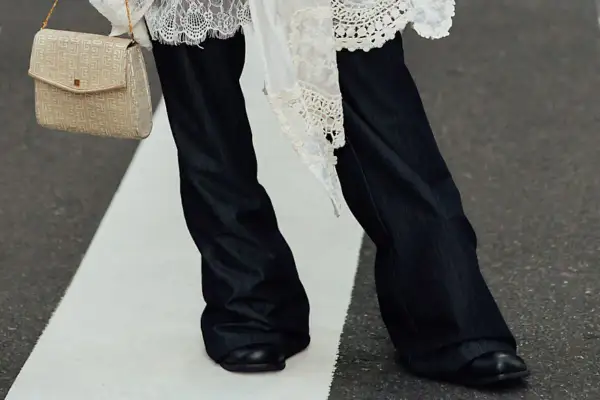 Eleganckie połączenie sukienki ze spodniami. Długie, ciemne dżinsy i biała, koronkowa narzutka tworzą stylowy look.