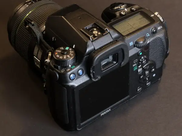 En närbild på en Pentax K5 systemkamera med objektivet på. Knappar och skärm syns tydligt.