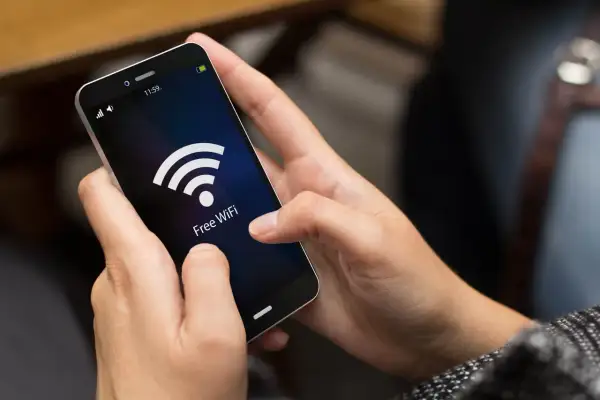 Dłonie trzymają smartfon z ikoną Wi-Fi i napisem "Free WiFi". Dowiedz się, jak sprawdzić zużycie internetu w telefonie, by kontrolować dane.