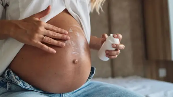 Manos aplicando crema en el vientre de una mujer embarazada. La crema, con un toque de rosa mosqueta, ayuda a cuidar la piel.