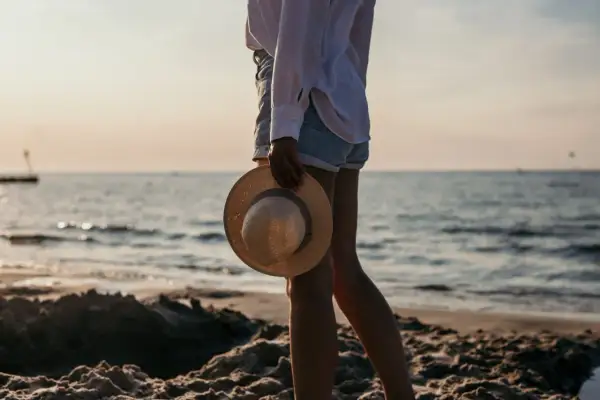 Sonnenuntergang am Kolberg Strand. Eine Frau hält einen Strohhut, während sie am Wasser entlang spaziert.