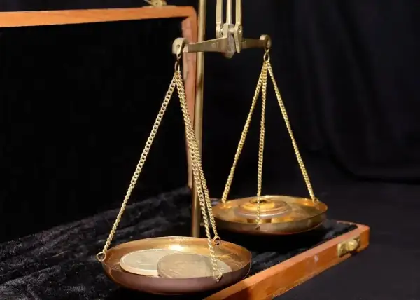 Złota waga szalkowa z monetami na jednej szalce i odważnikami na drugiej. Waga symbolizuje wartość, być może uncja złota.
