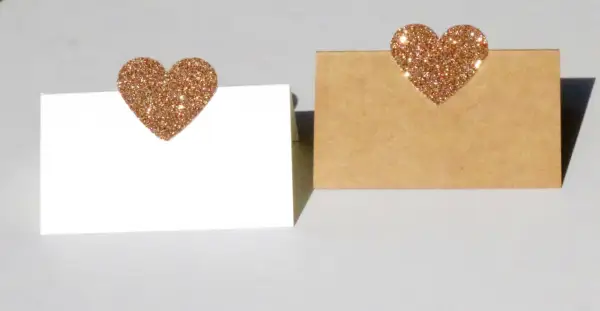 Segnaposto nozze d'oro fai da te: due cartoncini, uno bianco e uno kraft, decorati con cuori glitterati color oro.