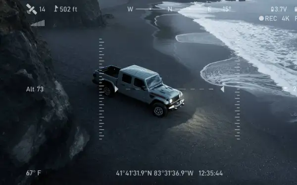 Un camion du futur gris, vu du ciel, roule sur une plage de sable noir. Les vagues de l'océan s'écrasent sur le rivage.
