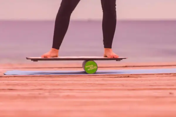Füße balancieren auf einem Wackelbrett über einer Rolle.