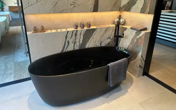 Baignoire noire en acrylique, prête pour un nettoyage. Un drap de bain gris est accroché.