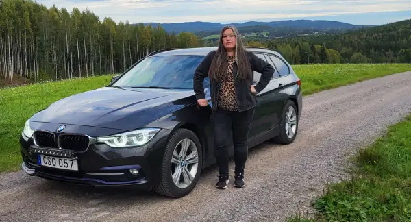 Kvinna vid en svart BMW kombi i svensk landsbygd. Kanske ett bmw b47 problem som gör att hon stannat här.