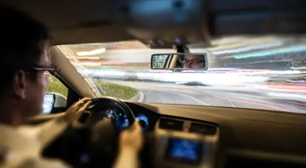 Conductor con gafas al volante de noche, con lluvia y luces de coches borrosas. El ASR de un coche ayuda a mantener la tracción en estas condiciones.