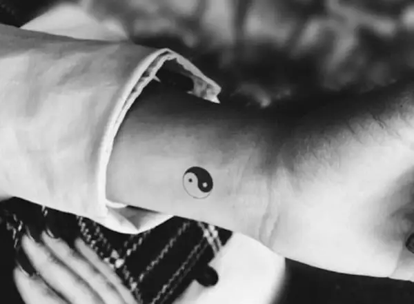 Mały tatuaż yin yang na nadgarstku. Symbolizuje równowagę i harmonię, a jego znaczenie jest głębokie.