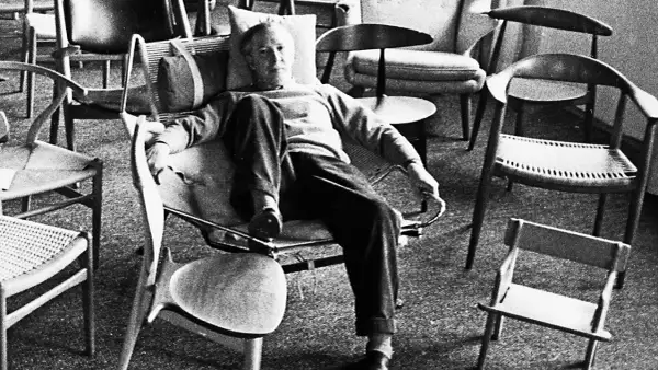 Hans J Wegner, a master of Danish design, relaxes amidst his iconic chairs, surrounded by his timeless creations.