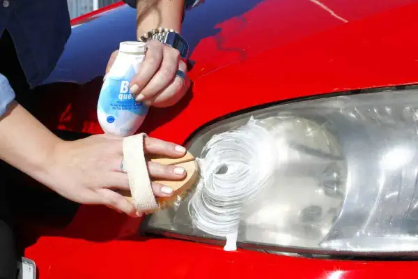 Manos limpiando un faro de coche con pasta blanca para pasar la ITV.