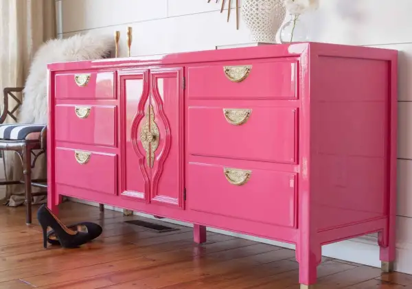 Comò rosa brillante con maniglie dorate, un esempio di come laccare un mobile già verniciato per un look audace.