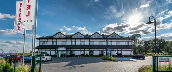 Hotel z białymi ścianami i czarnymi belkami, trzy gwiazdki na fladze, parking.