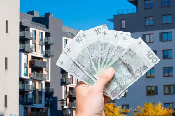Dłoń trzyma polskie banknoty 100 zł na tle nowoczesnych bloków mieszkalnych. To symbol ulgi mieszkaniowej i możliwości zakupu własnego lokum.