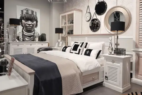 Sypialnia boho loft z łóżkiem, czarnymi lampami i portretem kobiety. Dekoracje ścienne dodają charakteru.