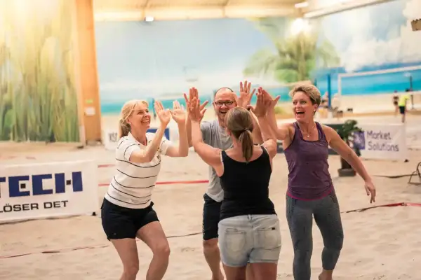 Fyra glada kollegor ger varandra high-fives på en sandstrand. Perfekta tips på aktiviteter med kollegor för teambuilding!