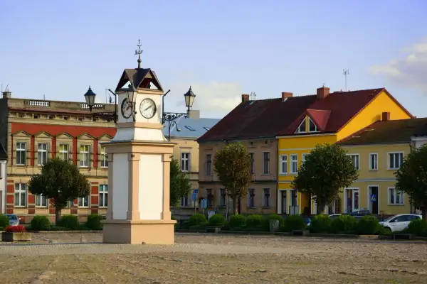 Rynek w **Lwówek Wlkp.** z zegarową wieżą po lewej i kolorowymi kamienicami w tle.