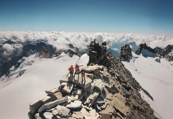 Des alpinistes atteignent le sommet rocheux, dominant un océan de nuages. Un panorama à couper le souffle, un véritable grand paradis.